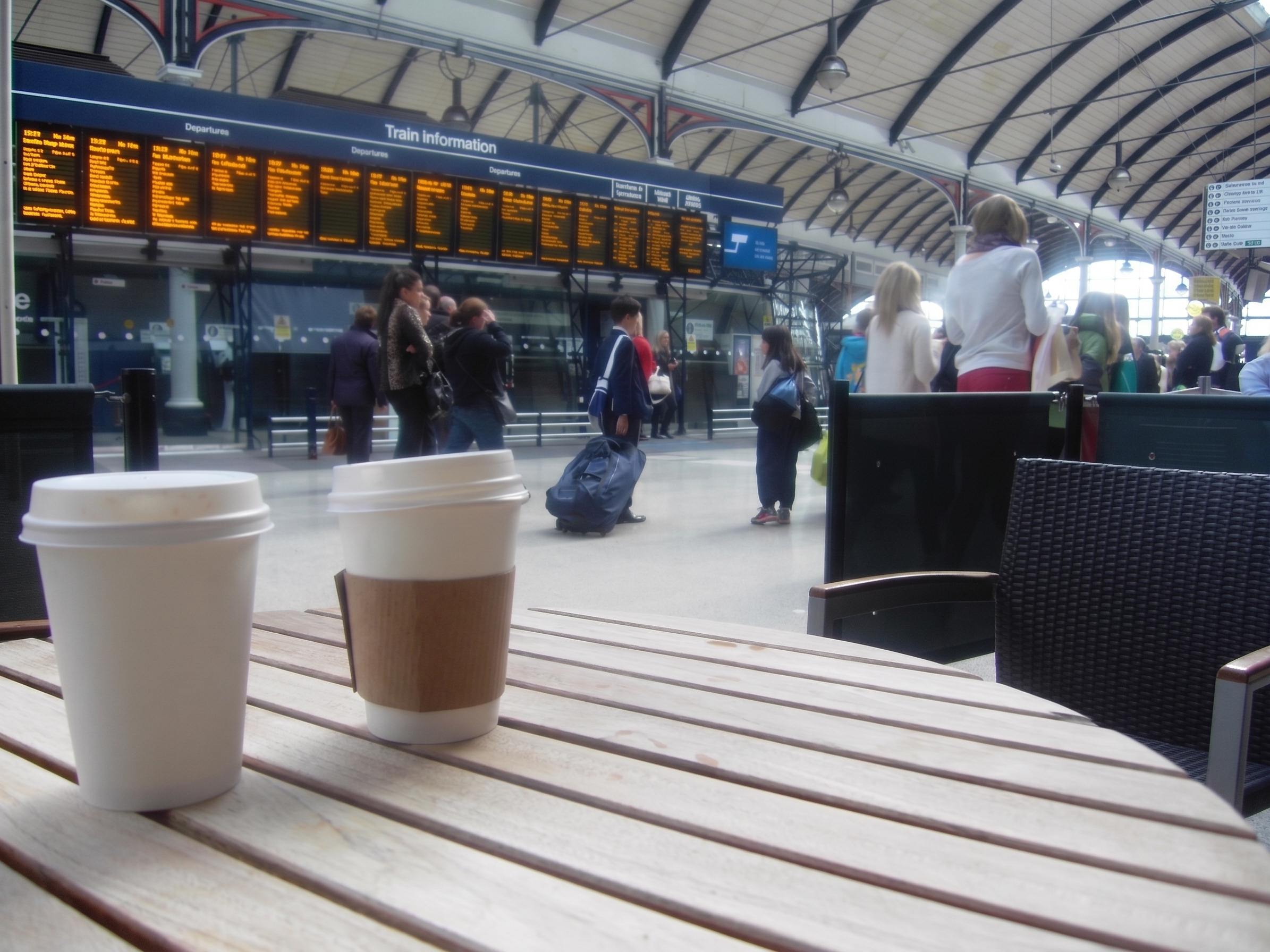 Coffee cups on a table inside a busy railway station.